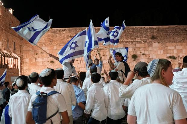 Young Jewish people wave Israeli flags near the Western Wall in Jerusalem